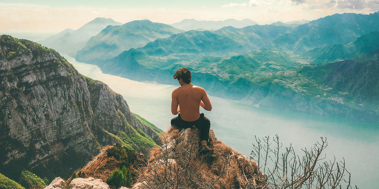 Young man sits on a rocky outcrop overlooking a beautiful wilderness landscape.