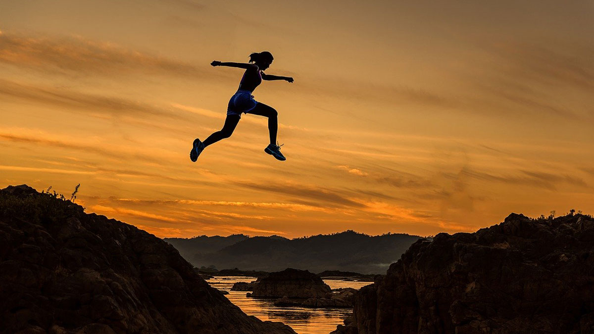 A woman leaps across a gorge.